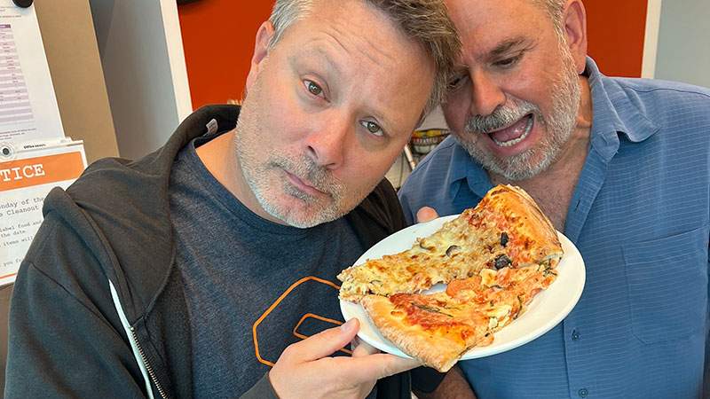 Two employees posing with a slice of pizza