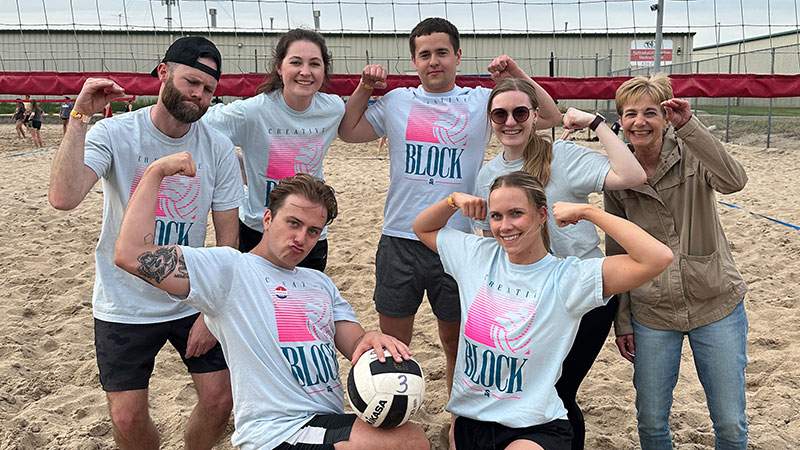 Beach volleyball team members posing and flexing on the sand court